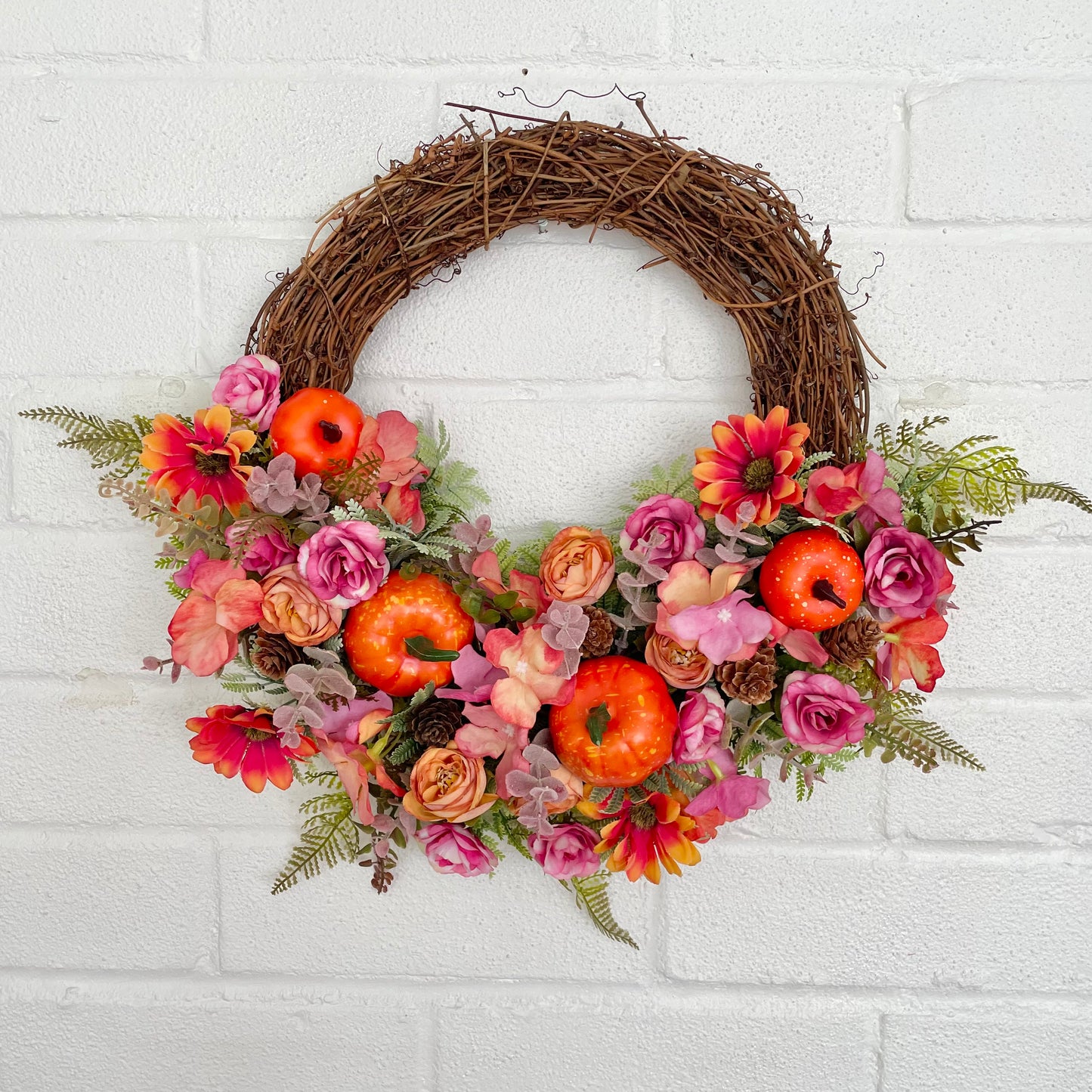 Bright autumn door wreath with pink and orange flowers, pumpkins and pinecones