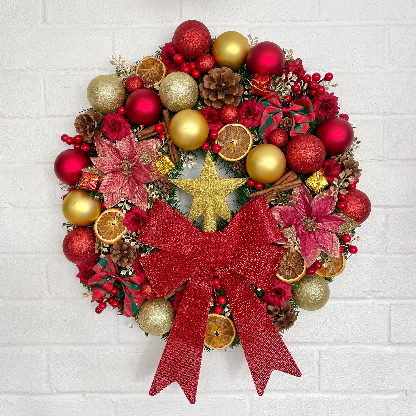 Huge Christmas wreath filled with red and gold decorations, pine cones, oranges, cinnamon and berries