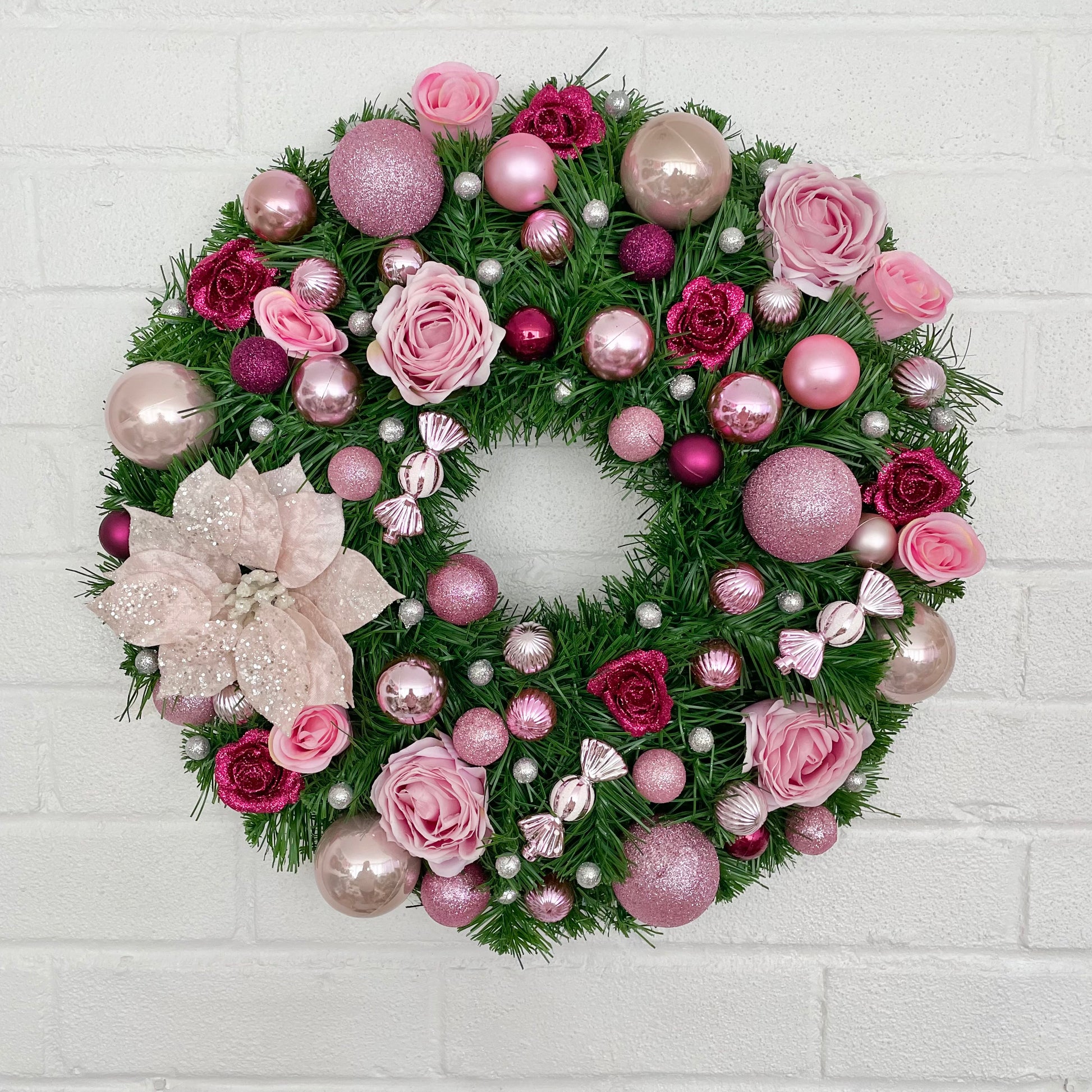 Pink Christmas wreath with baubles, roses and poinsettia 